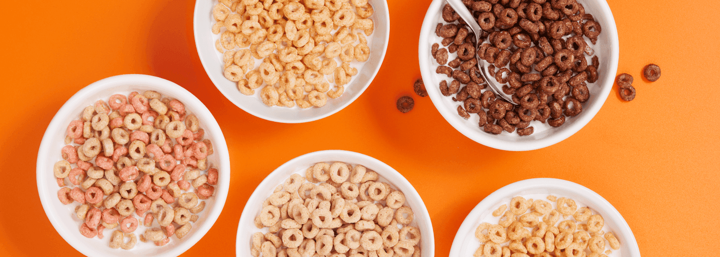 Bowls of various types of cheerios breakfast cereals on an orange background.