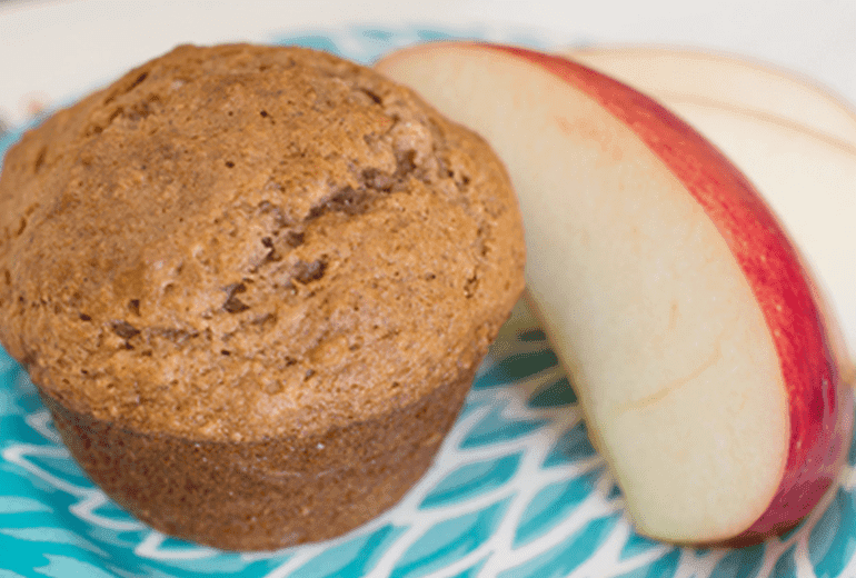 A Cheerios Applesauce Muffin with slices of apple next to it on a plate.