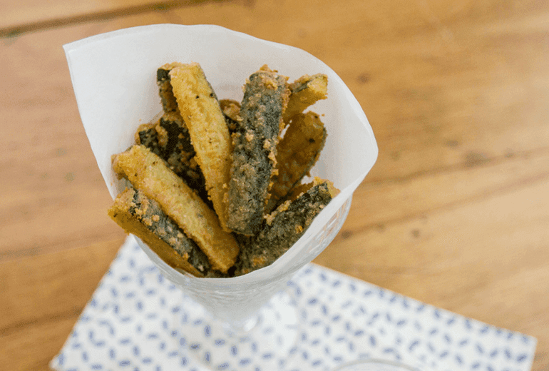 Baked zucchini sticks coated in crushed Cheerios in a glass with baking paper wrapped around them.