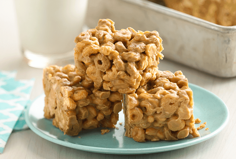 Three No-Bake Peanut Butter Bars made with Cheerios Protein Cinnamon Almond cereal stacked on a plate.