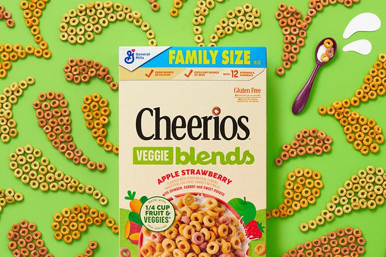 Una caja de vegetales Cheerios, manzana, fresa, mezcla cereales sobre un fondo verde con patrón de cereales.