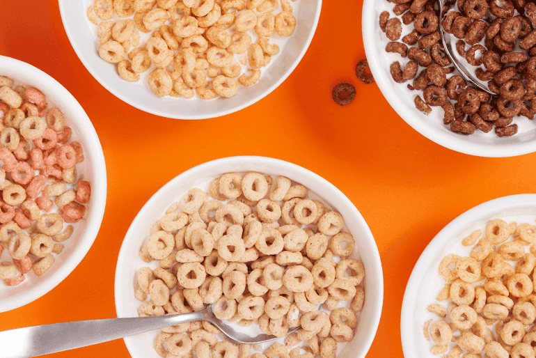 Cuencos de varios tipos de cereales de desayuno cheerios sobre un fondo naranja.