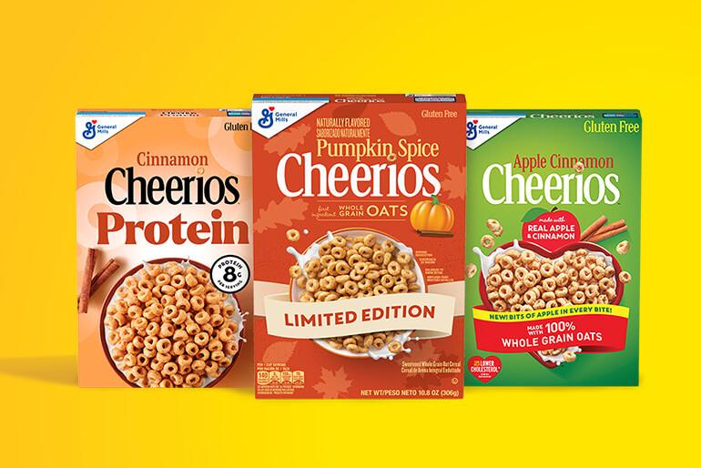 Three boxes of Cheerios cereal are displayed. From left to right: Cinnamon Cheerios Protein with 8g of protein, Pumpkin Spice Cheerios labeled as 'Limited Edition', and Apple Cinnamon Cheerios made with real apple and cinnamon, featuring whole grain oats. All boxes are marked as gluten-free.