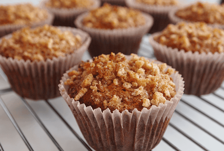 A collection of banana muffins made and topped with crushed Cheerios on a metal grill.