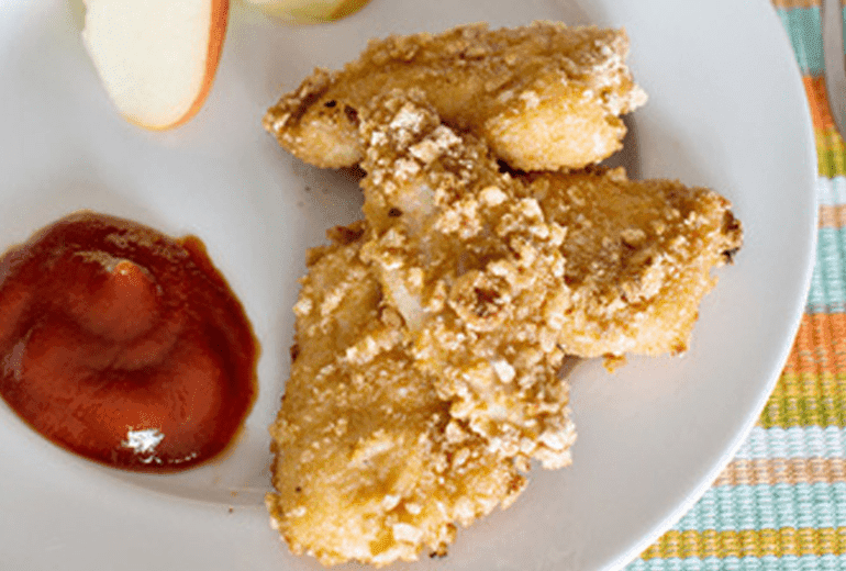 Chicken nuggets breaded with gluten free Cheerios on a plate with a dollop of ketchup.